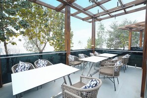 An outdoor patio with wicker furniture and glass railings, overlooking a body of water. - ODHNI DAM RESORT (Banka)