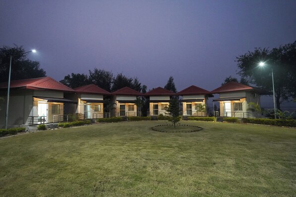 A row of four hotel buildings with red roofs, a central lawn, and a small tree. - ODHNI DAM RESORT (Banka)
