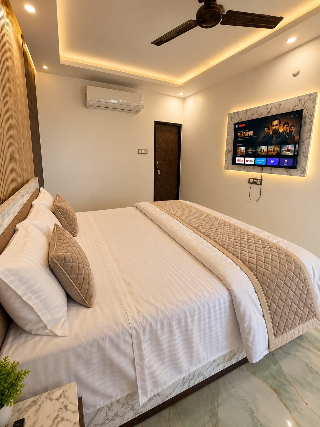 A modern hotel room with a bed, a ceiling fan, an air conditioning unit, a television mounted on the wall, and a marble-patterned floor.