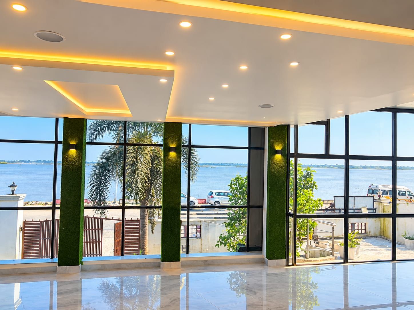 A spacious interior with large windows offering a view of the water and palm trees.