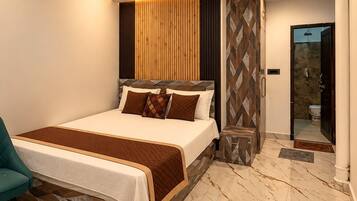 Une chambre moderne avec un grand lit, un ventilateur de plafond et une salle de bain visible à travers une porte ouverte.