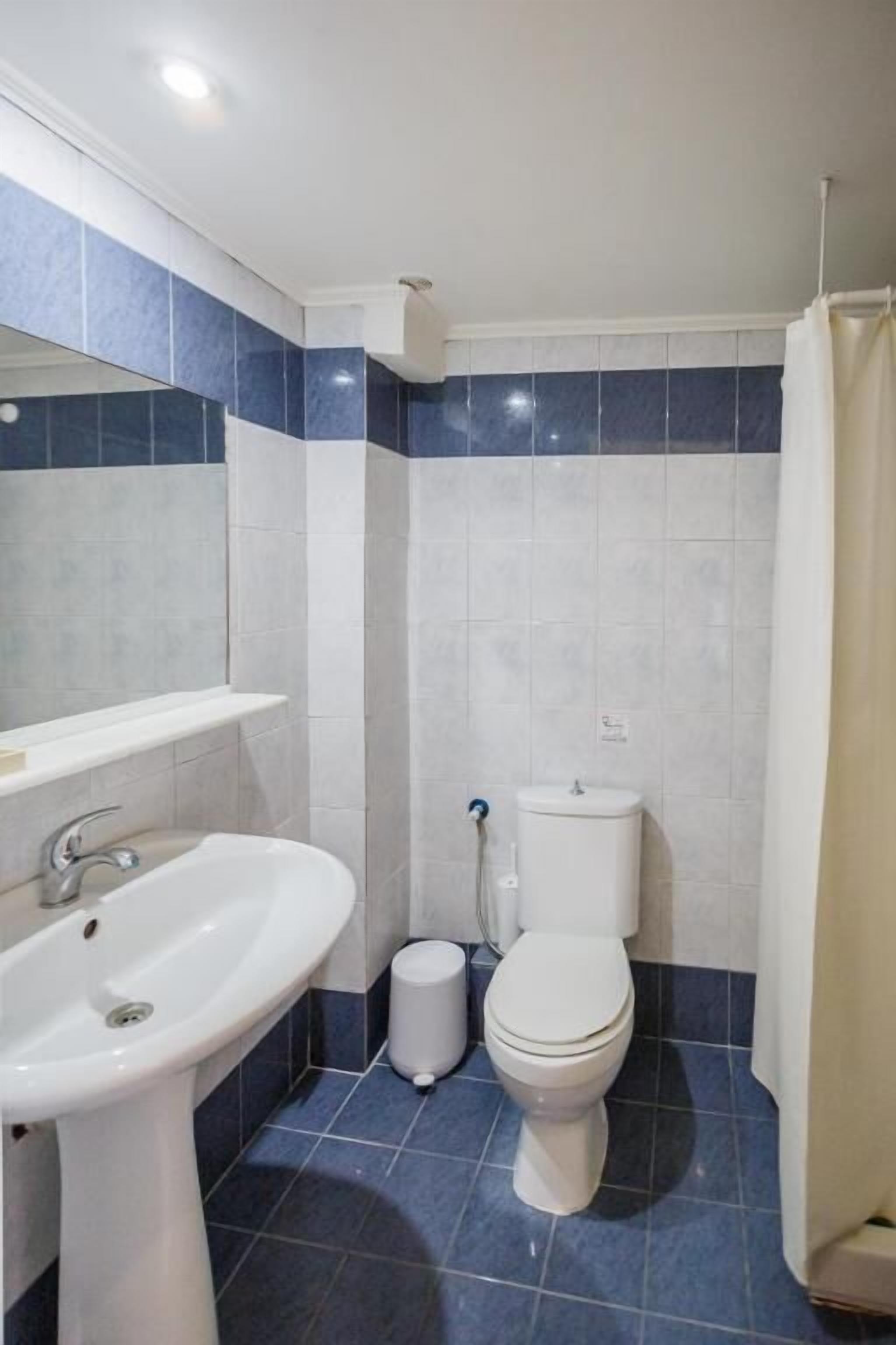 Un baño con lavamanos, inodoro y un cubo de basura blanco.