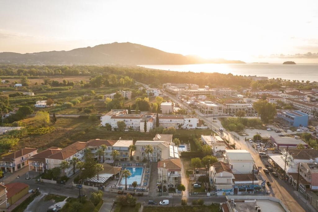 An aerial view of a coastal town with residential buildings, a swimming pool, and a road leading to the sea.