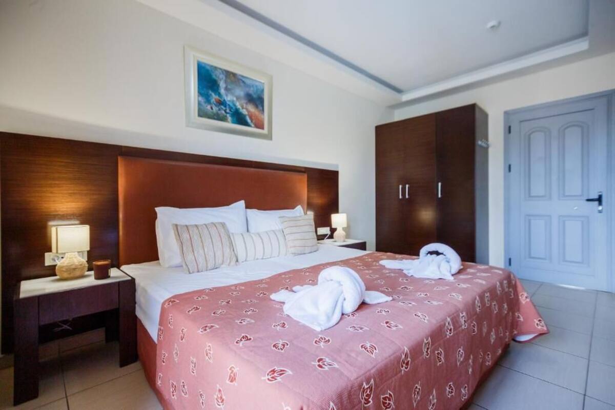 A hotel room with a large bed, a wooden headboard, a nightstand with a lamp, and a wardrobe.