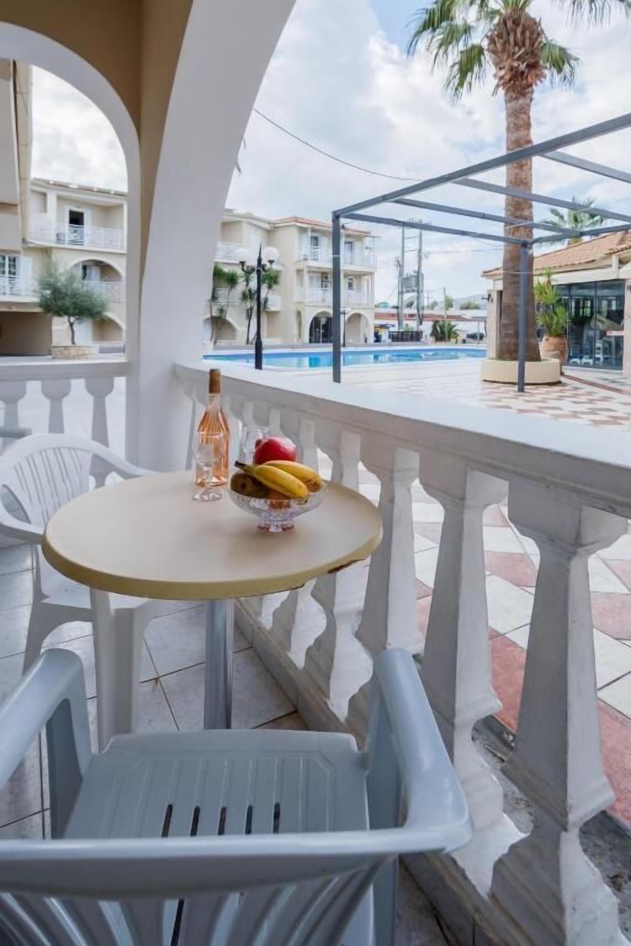 A balcony with a round table, a bottle, and a bowl of fruit.