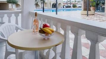 A balcony with a round table, a bottle, and a bowl of fruit.
