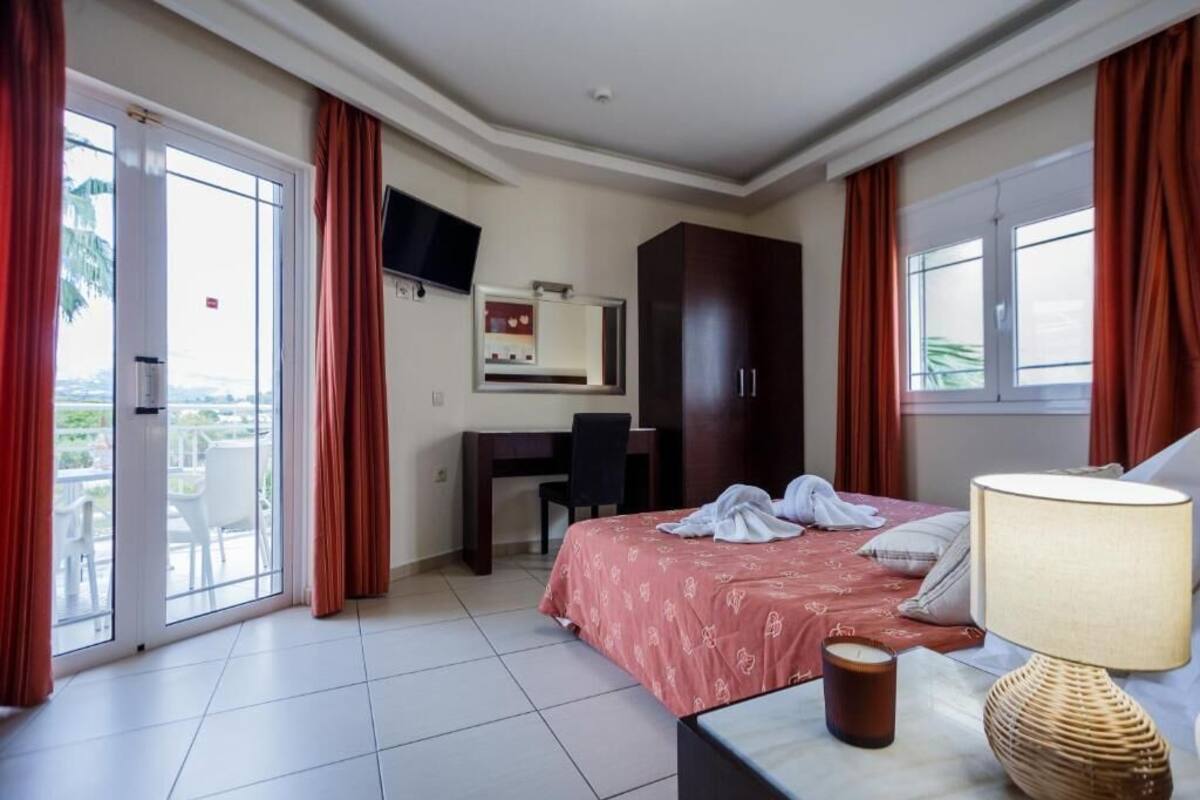 A hotel room with a bed, a desk, a TV, and a balcony with red curtains.