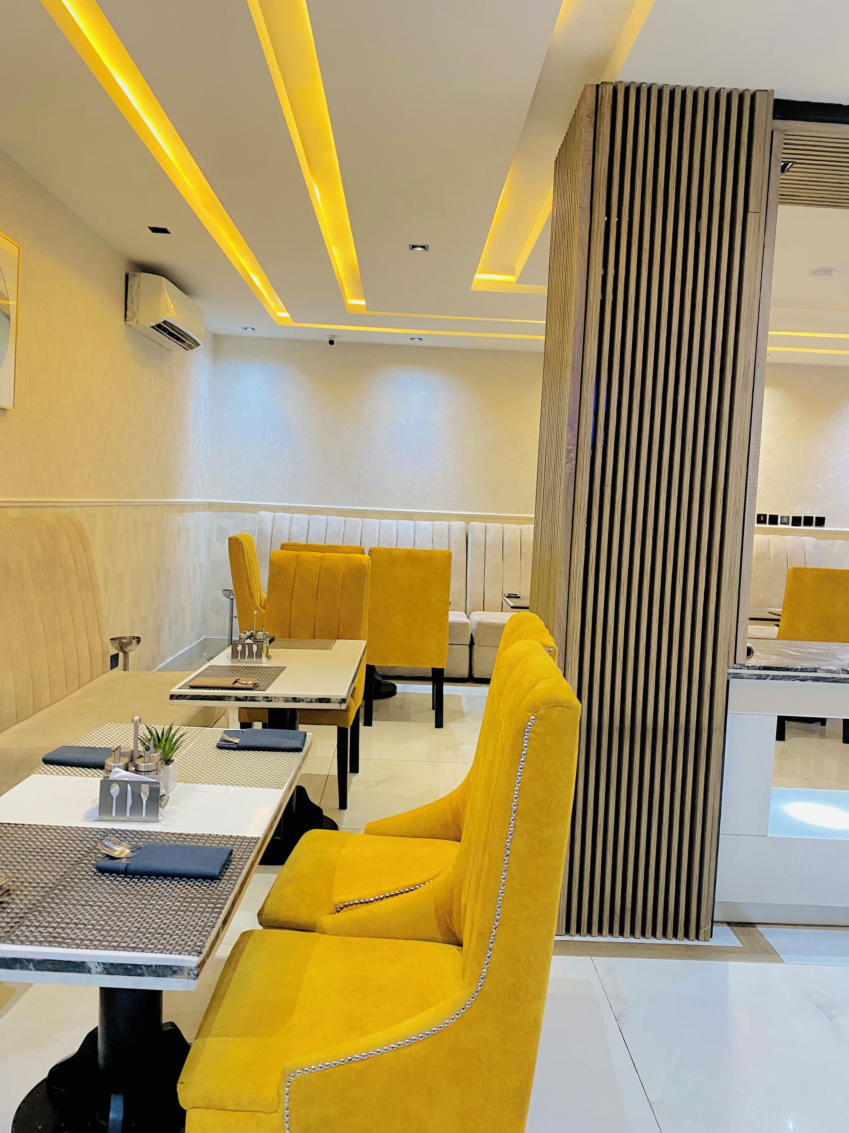 Un comedor moderno con sillas tapizadas en color amarillo, una mesa central y un diseño contemporáneo con luminarias lineales.