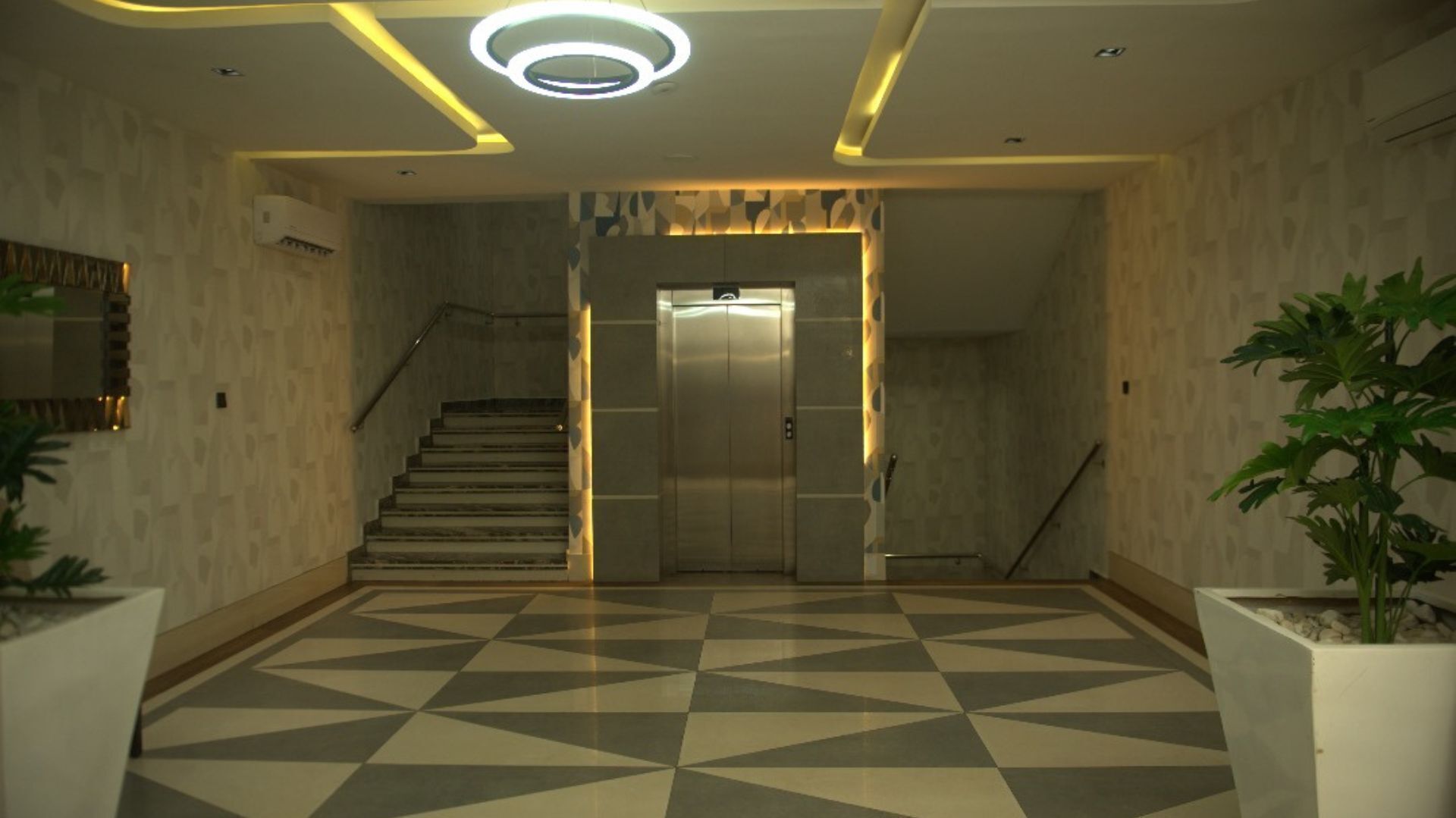 A modern lobby with a geometric patterned floor, a staircase, and an elevator.