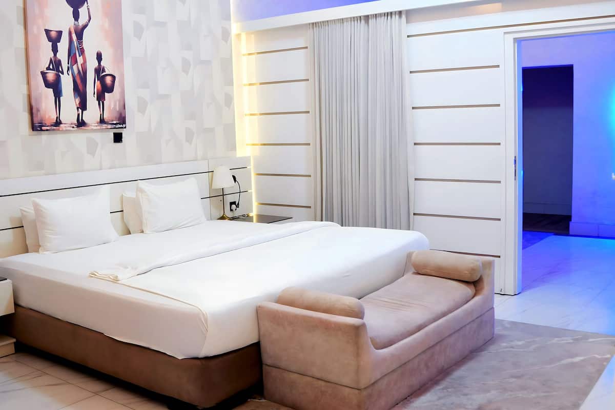 A modern hotel room with a large bed, a bedside table, a lamp, and a painting on the wall.