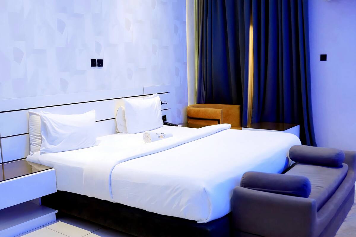 A modern hotel room with a neatly made bed, a small sofa, and a nightstand.