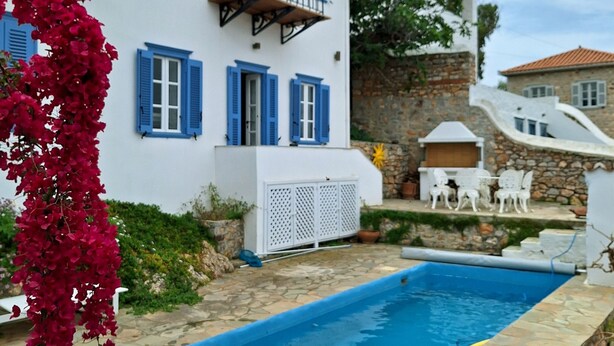 A white building with blue shutters and a stone pool.