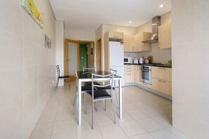A modern kitchen with a dining table and chairs, a microwave, oven, and a stainless steel range hood. - Apartment 'T2 Duplex - S Pedro 3' with Sea View, Wi-Fi and Air Conditioning (Ponta Delgada)