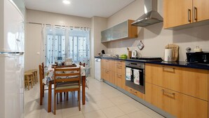 Eine Küche mit Holzausbau, einem Esstisch mit Stühlen, einem eingebauten Backofen und einem Fenster mit Jalousien.