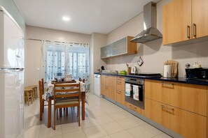 A kitchen with wooden cabinets, a dining table with chairs, a built-in oven, and a window with blinds. - Apartment 'T3 - Sao Pedro 2' with Sea View, Wi-Fi and Air Conditioning (Ponta Delgada)