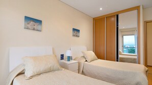 Ein Hotelzimmer mit zwei Betten, einem Nachttisch mit Lampe, einem kleinen Gemälde und einer Schiebetür, die auf einen Balkon führt.