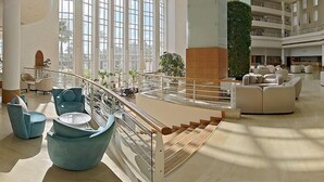 Een ruime lobby met een centrale trap, grote ramen en moderne zithoeken.