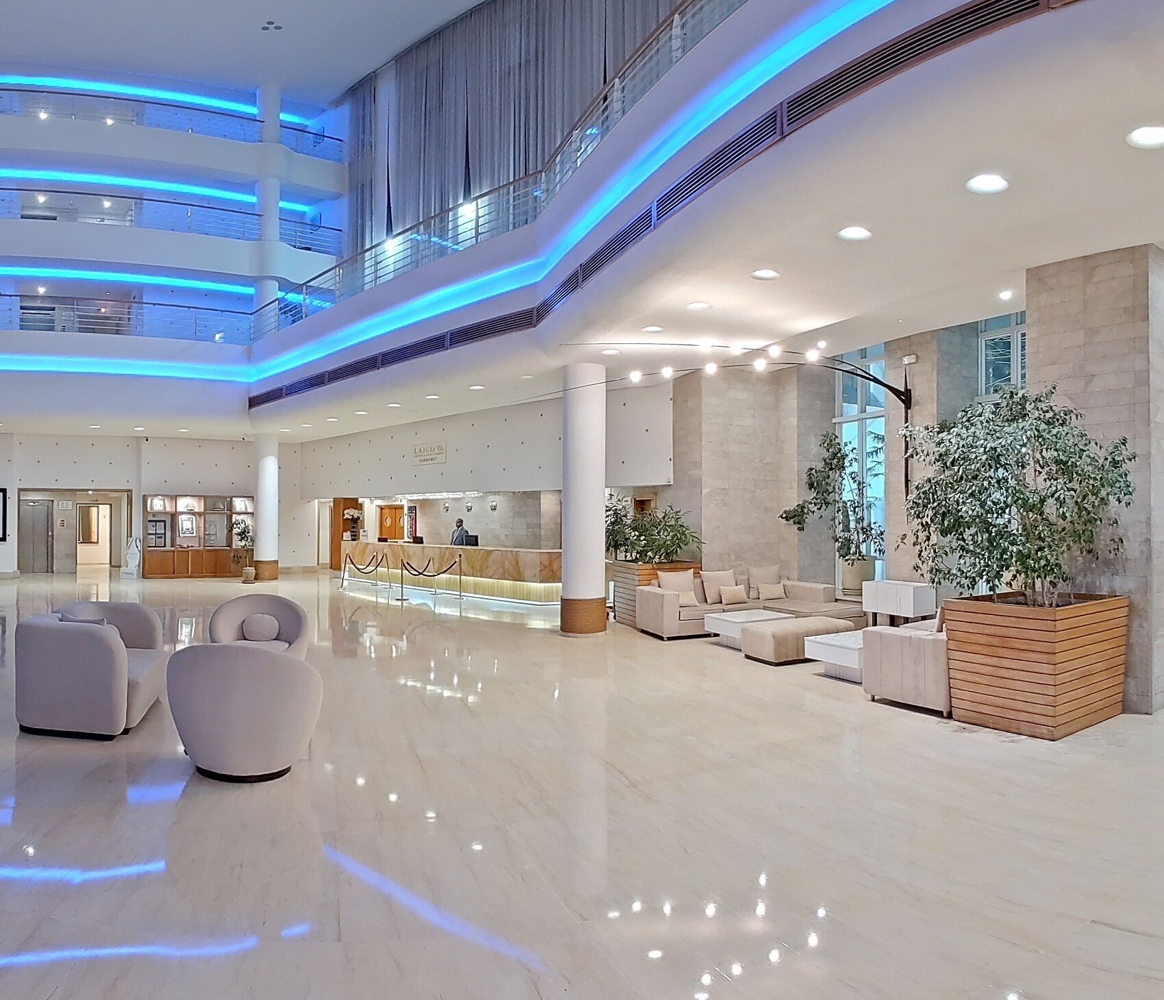 Een ruime lobby met een receptiebalie, een zithoek en een grote plant.