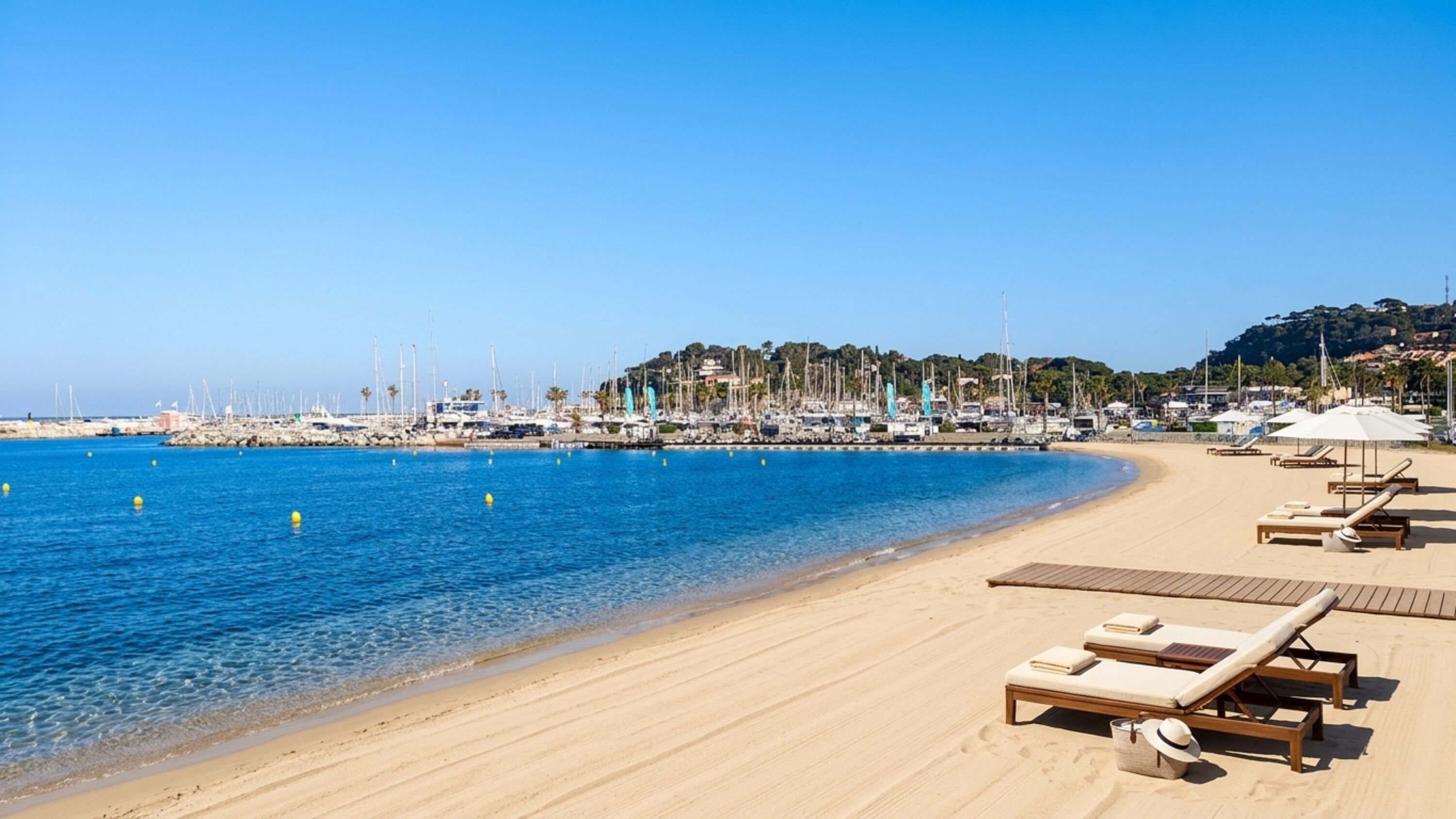 A beach with clear blue water, a sandy shore, and lounge chairs.