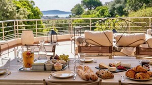 A table set with breakfast items, including croissants, cheese, and fruit, overlooking a scenic landscape. - CASA-Stella Maris villa avec vue sur la mer (Cavalaire-sur-Mer)