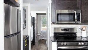 A compact kitchen with a stainless steel refrigerator, a microwave, and a built-in oven. - Mountain Tiny Home in Blue Ridge Mountains (Copperhill)