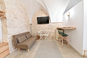 Ein gemütlicher Wohnbereich mit einer Steinwand, einem Flachbildfernseher, der über einem Holztisch mit Stühlen angebracht ist, einer Couch und einem kleinen Holzschemel.