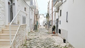 Una estrecha calle adoquinada flanqueada por edificios blancos con balcones y una escalera que lleva a un piso superior.