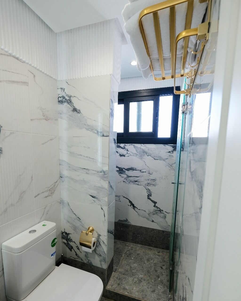 Un bagno con il water, pareti in marmo, una doccia con porte in vetro e una finestra.