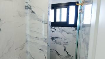 Un bagno con il water, pareti in marmo, una doccia con porte in vetro e una finestra.