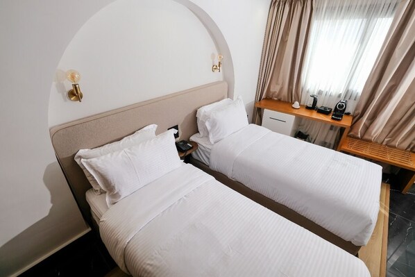 A hotel room with two single beds, a wooden nightstand, a desk, and a window with curtains. - chic hotel rabat (Rabat)