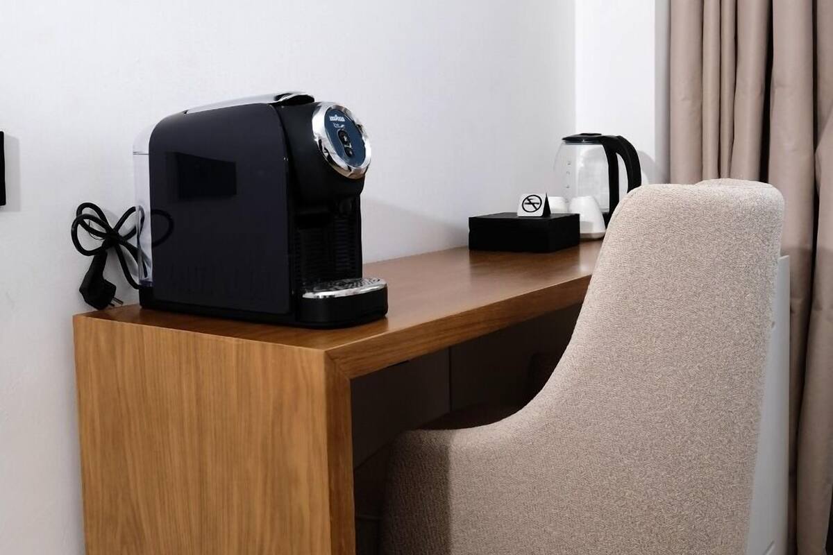 A modern room with a wooden desk, a beige chair, a coffee maker, a kettle, and a TV mounted on the wall.