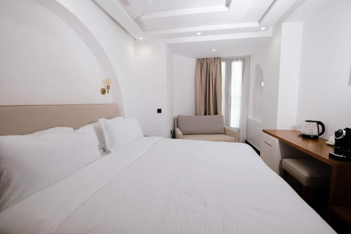 A modern hotel room with a large bed, a sofa, a desk, and a coffee maker.