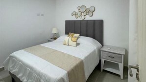 A bedroom with a bed, bedside tables, a lamp, and a decorative wall piece. - Serena Village E5 AP 203 (Punta Cana)