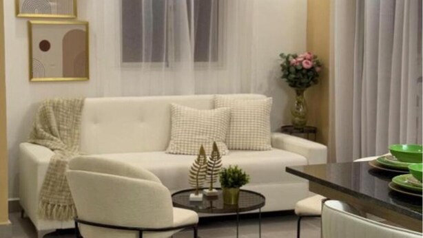 A modern living room with a white sofa, a round coffee table, and a dining area with a black table and green bowls. - Serena Village E5 AP 203 (Punta Cana)
