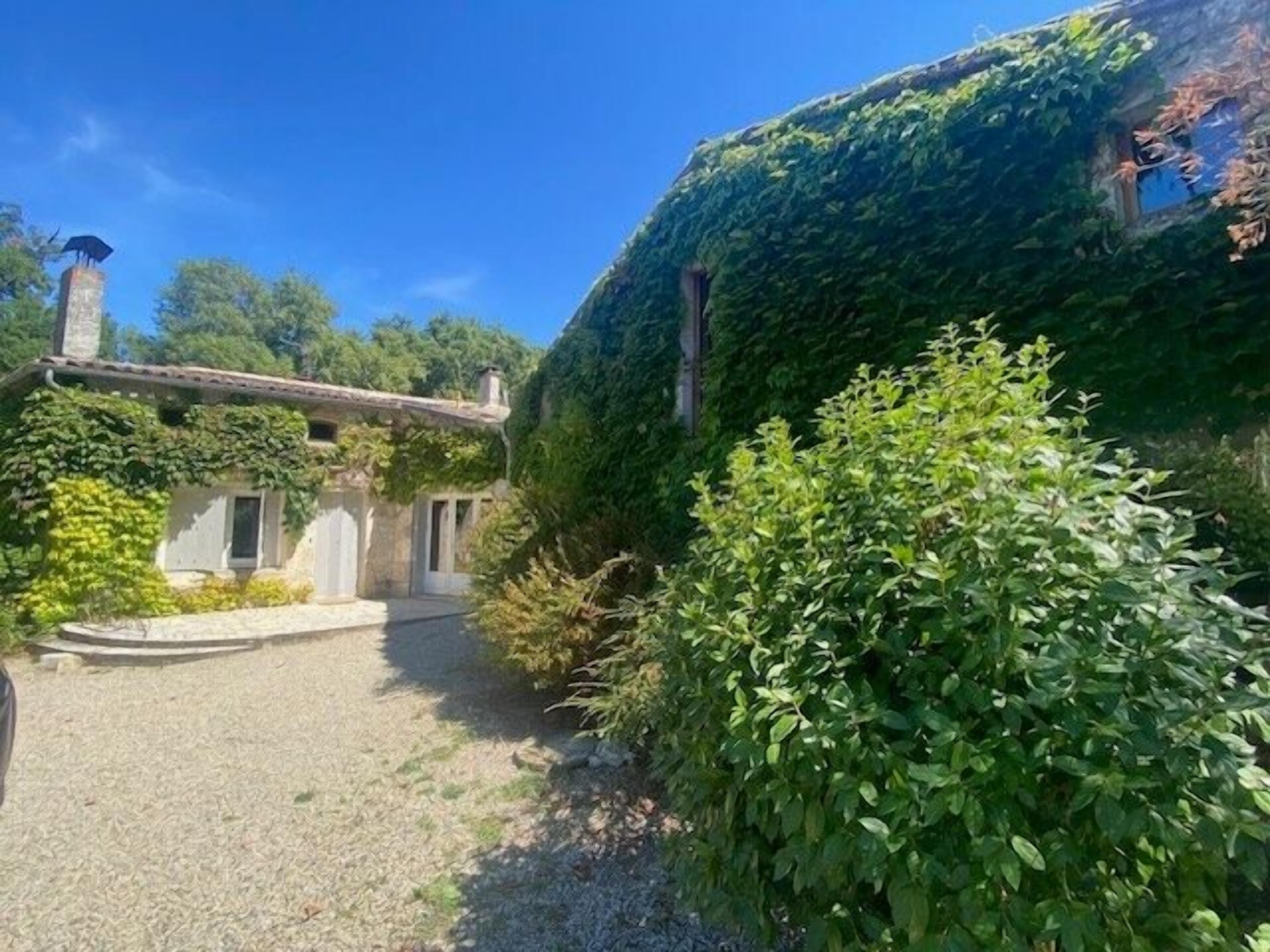 Ein rustikales Steinhaus mit Efeu bewachsenen Mauern, einem Kieshof und einem großen Busch im Vordergrund.