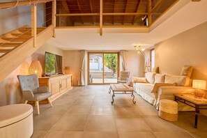 A spacious living area with a wooden staircase, a sofa set, a coffee table, and a television on a wooden cabinet. - Gîte des 3 Sourires - Grand Jardin Privé (Eynesse)