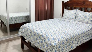 Une chambre avec un lit en bois, une porte-fenêtre coulissante, une fenêtre avec des rideaux bruns et un appareil de climatisation fixé au mur.