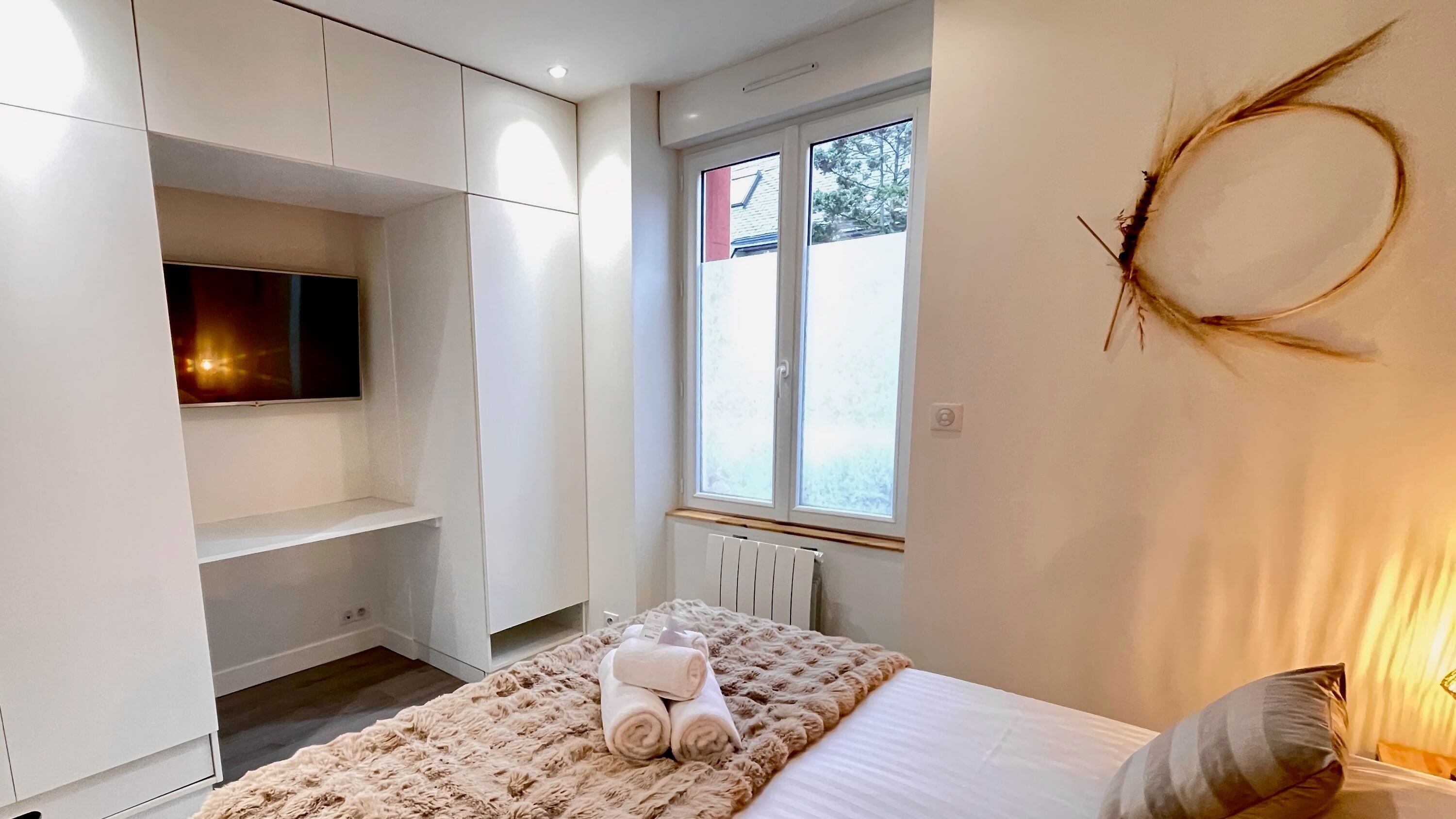 Une chambre à coucher avec un lit, un téléviseur fixé au mur et une fenêtre donnant sur les arbres.