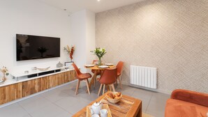 Een moderne woonkamer met een flatscreen televisie, een houten eettafel en oranje stoelen.