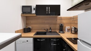 Een compacte keuken met een magnetron, een koelkast met dubbele deuren, een inbouwvaatwasser en een houten aanrechtblad.