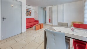 Ein modernes Wohnzimmer mit einem roten Sofa, einem Esstisch mit Stühlen und einer Küche im Hintergrund.