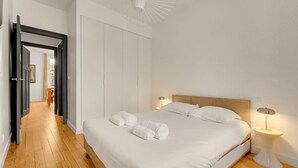 Ett sovrum med trägolv, en säng med vita sängkläder, ett sängbord med en lampa och en garderob.