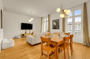 Un salon moderne comprenant un coin repas, un plancher en bois, un téléviseur à écran plat et de grandes fenêtres avec des rideaux.