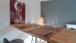 Un comedor con una mesa de madera dispuesta para dos, cristalería transparente y una botella decorativa.