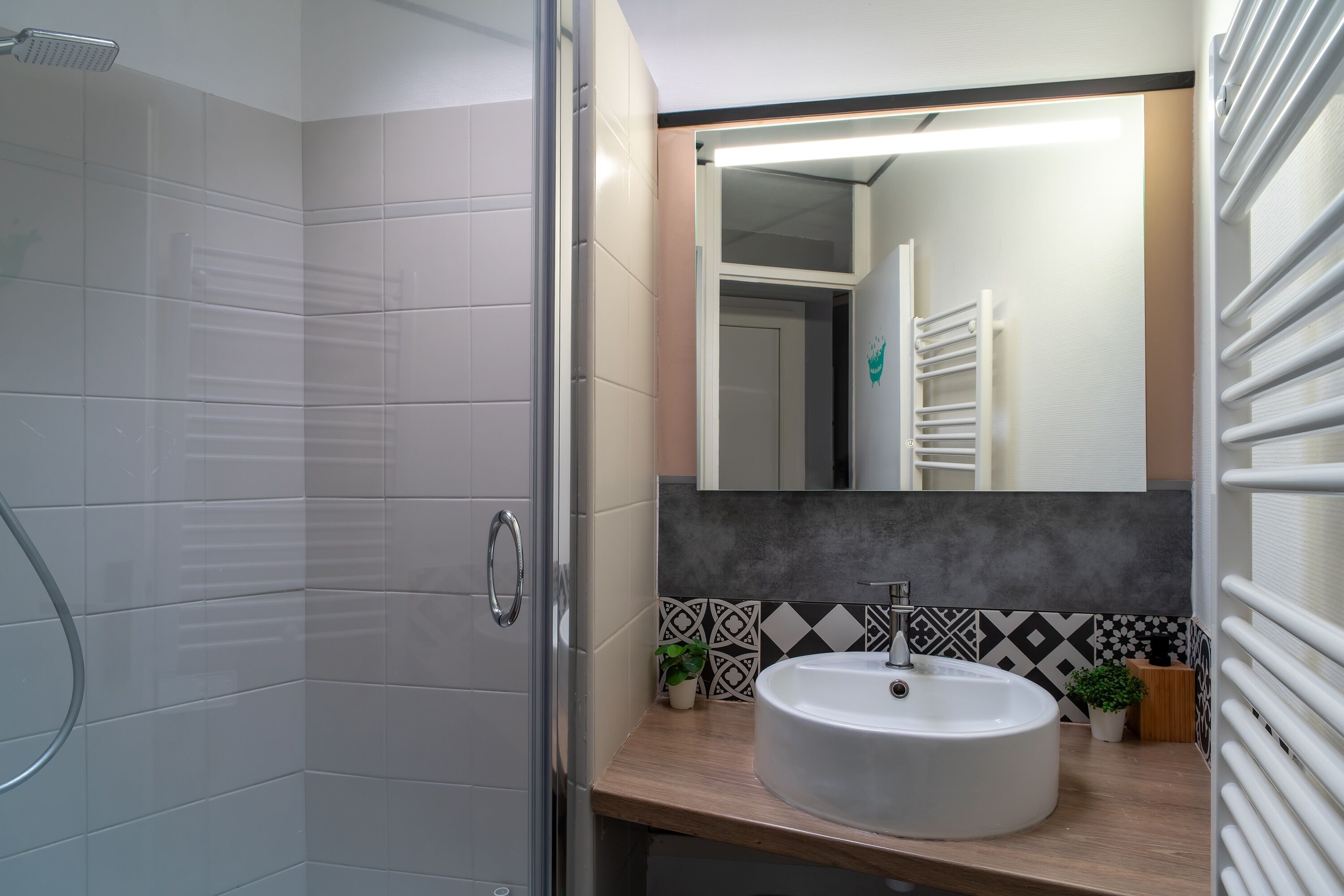 Un baño con cabina de ducha de vidrio, un lavamanos blanco de diseño moderno y un espejo con un elegante panel de pared geométrico.