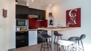 Cocina compacta con horno integrado, microondas y cafetera. Hay dos taburetes de bar y una pequeña mesa de comedor.