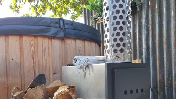 Un jacuzzi, un calentador de metal y una cesta de mimbre con leña.