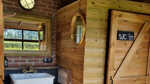 Un baño de madera rústico con lavamanos, espejo y una puerta que indica 'WC'.