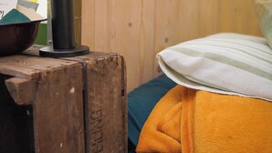 Un interior de madera con una cama, un espejo redondo y una lámpara sobre una mesa de madera.