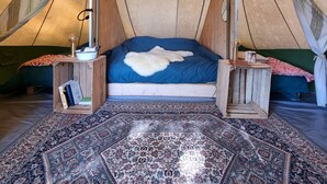Una habitación con tienda de campaña acogedora, con una cama, un tapete estampado y mesitas de noche de madera.